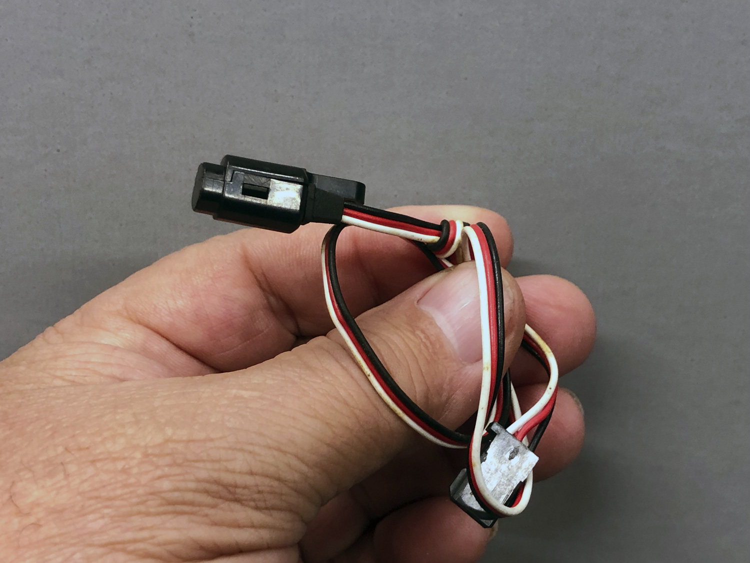 Close up of a hand-held Hall-effect sensor with overhand knot tied in the lead denoting it is defective