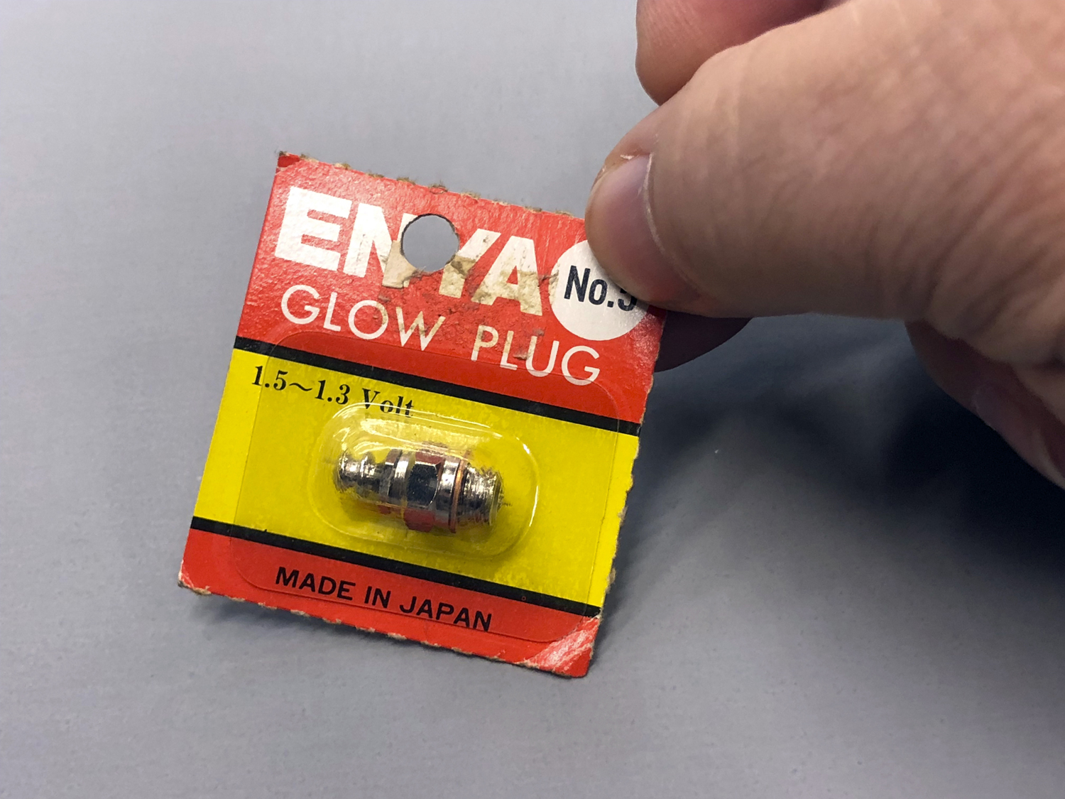 - Close up hand holding an Enya No. 3 glow plug within the packaging