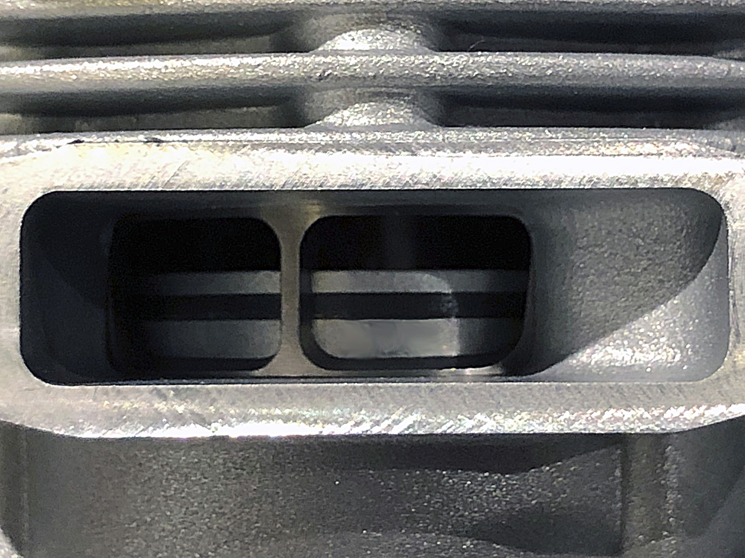 Close up look through the exhaust port of an OS MAX helicopter engine focused on the cast iron piston ring fitted near the top of an aluminum piston