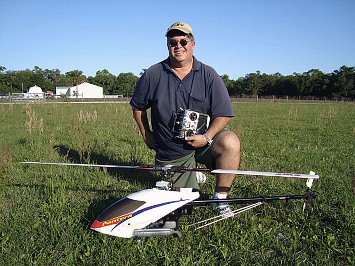 Photo of John kohn kneeling behind his pantera P6 in a grassy field on a cloudless blue afternoon