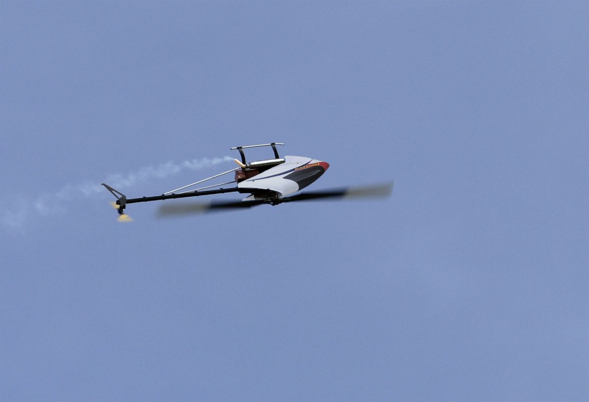 Photo of a Pantera P6 model helicopter flying left-to-right captured against a cloudless blue sky frozen midway through a roll